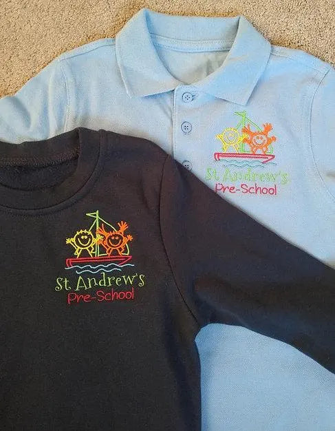 Light blue polo shirt and black long-sleeve shirt with 'St. Andrew's Pre-School' logo on a beige surface.