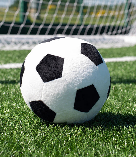 Plush soccer ball on a grass field with a goal in the background