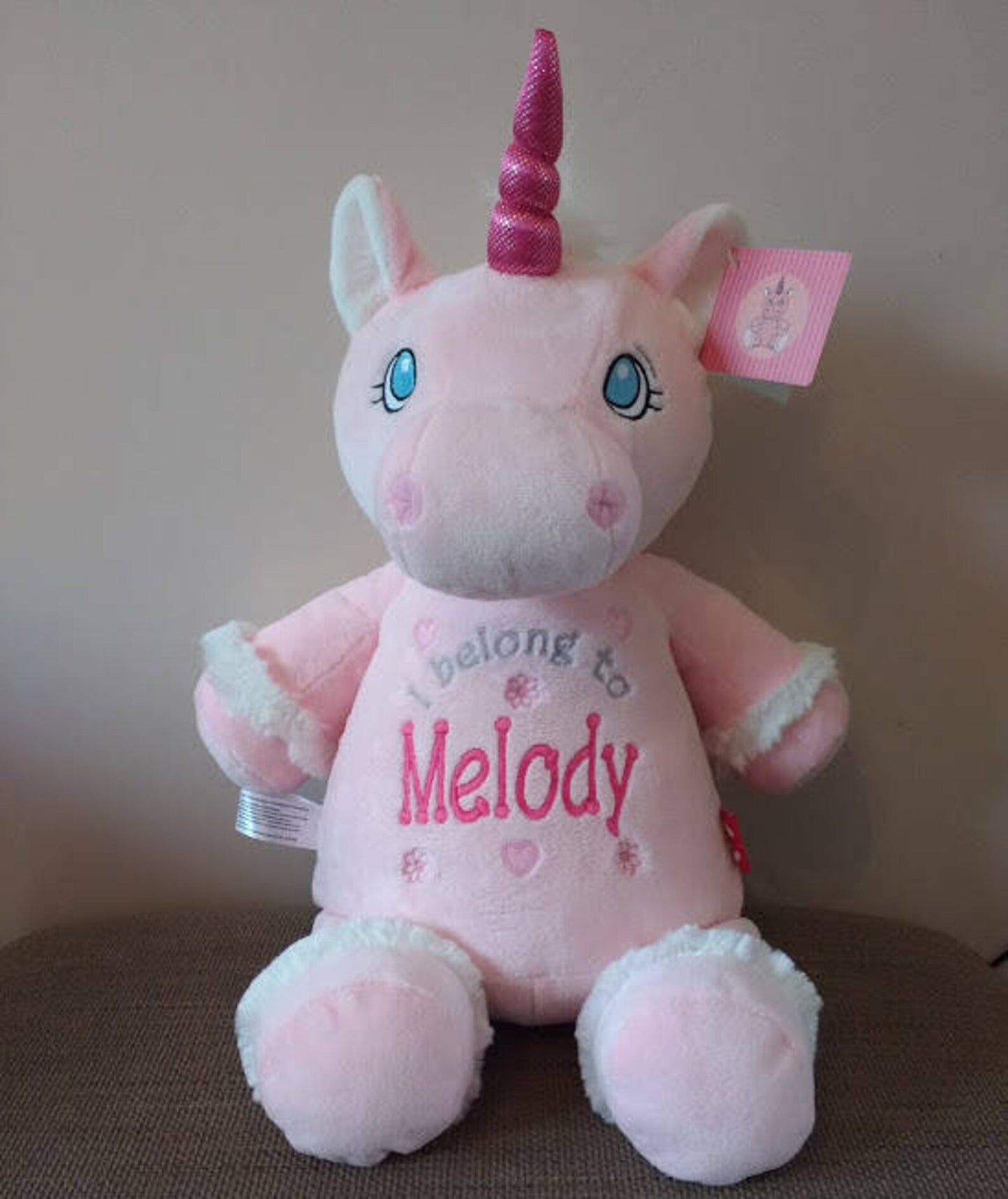 Pink unicorn plush toy with a name tag on a neutral background