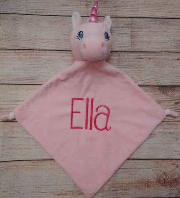 Pink unicorn plush toy with 'Ella' embroidered on a wooden surface
