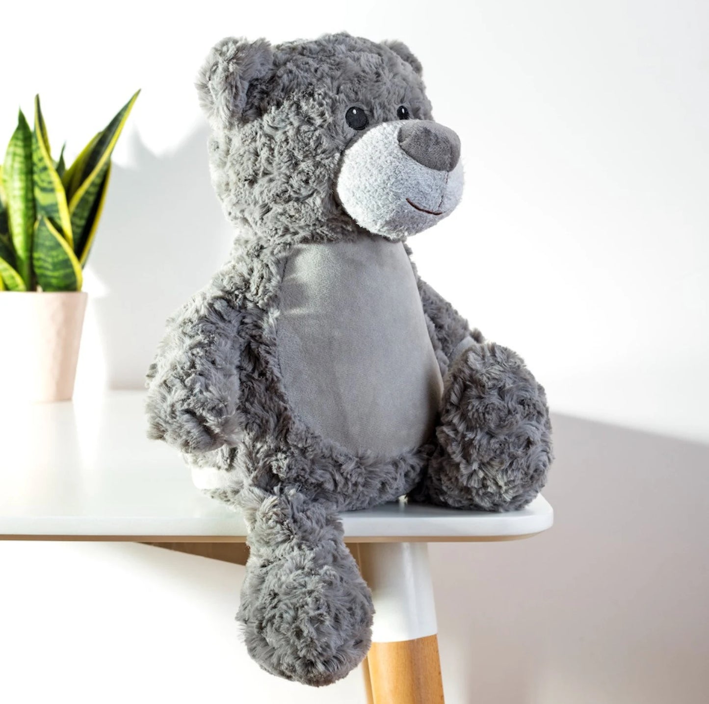Gray teddy bear on a white surface with a plant in the background
