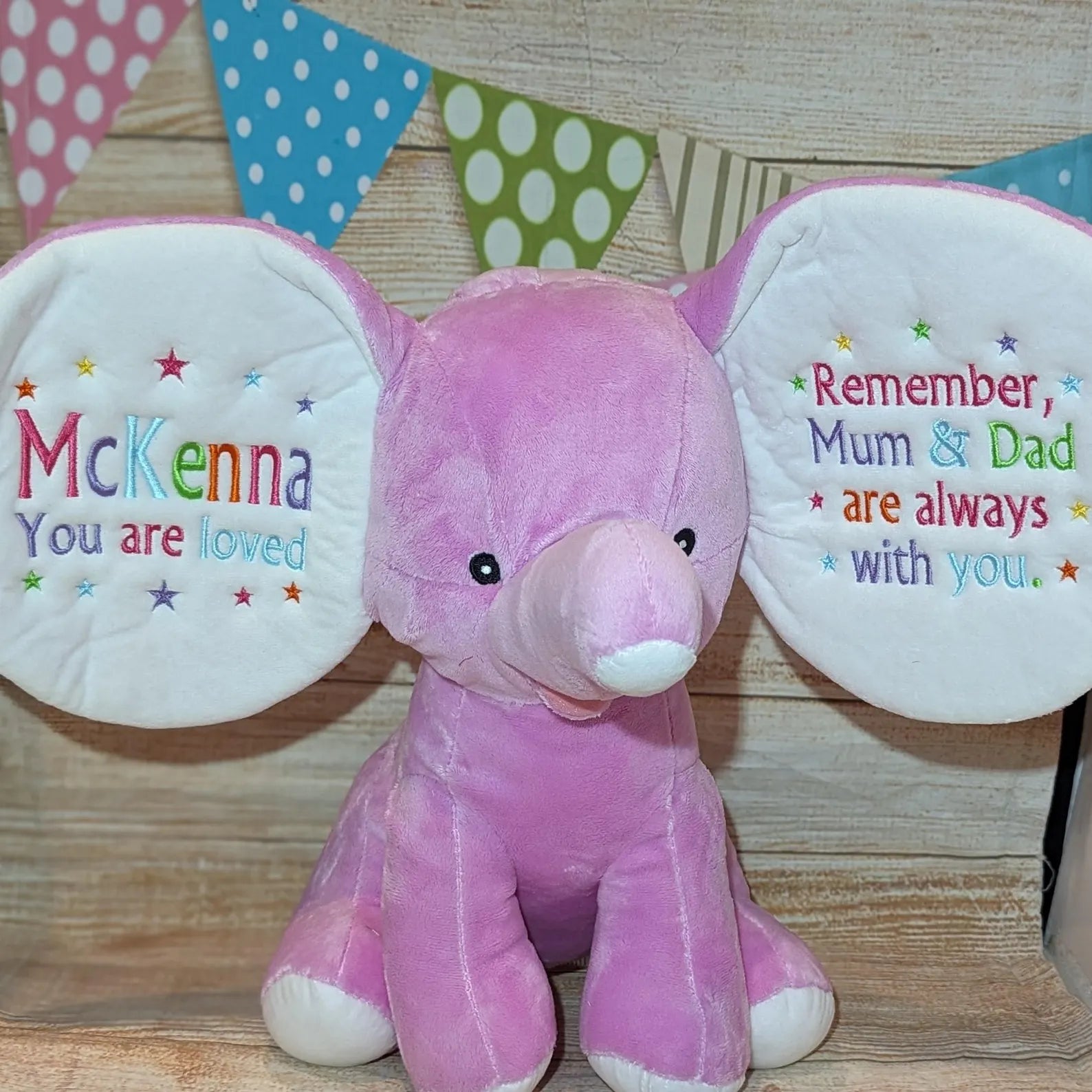 Pink plush toy with embroidered text on a wooden background