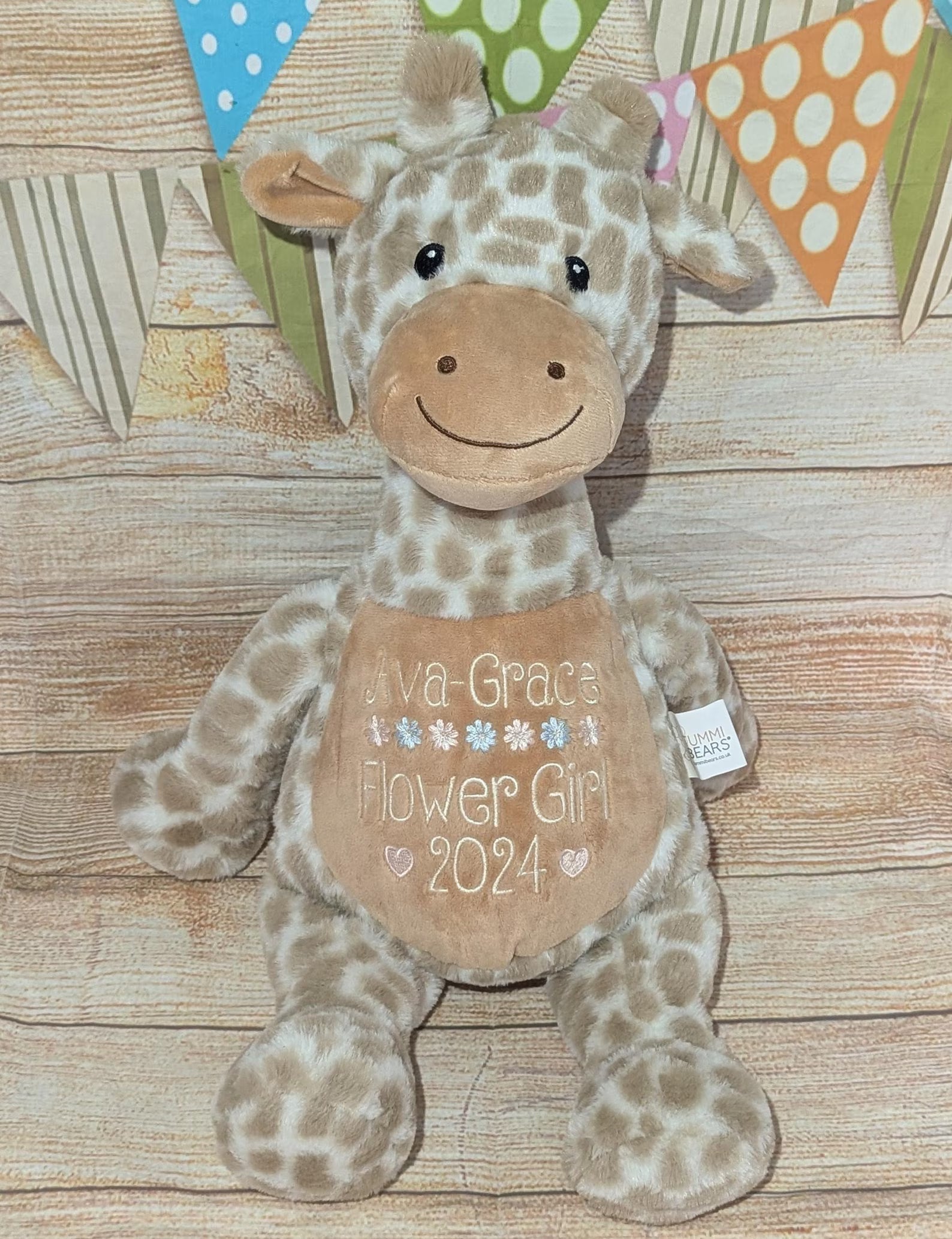 Plush giraffe toy with personalized message on a wooden surface with colorful flags in the background