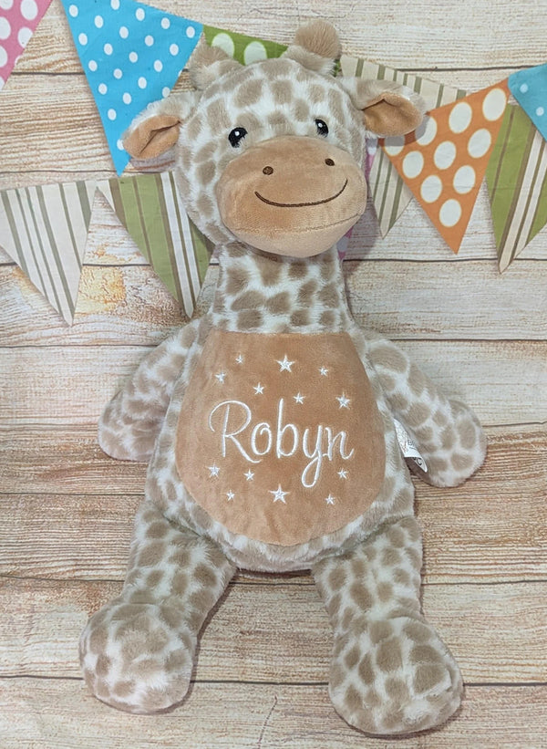 Plush giraffe toy with 'Robyn' on a wooden surface with colorful flags in the background