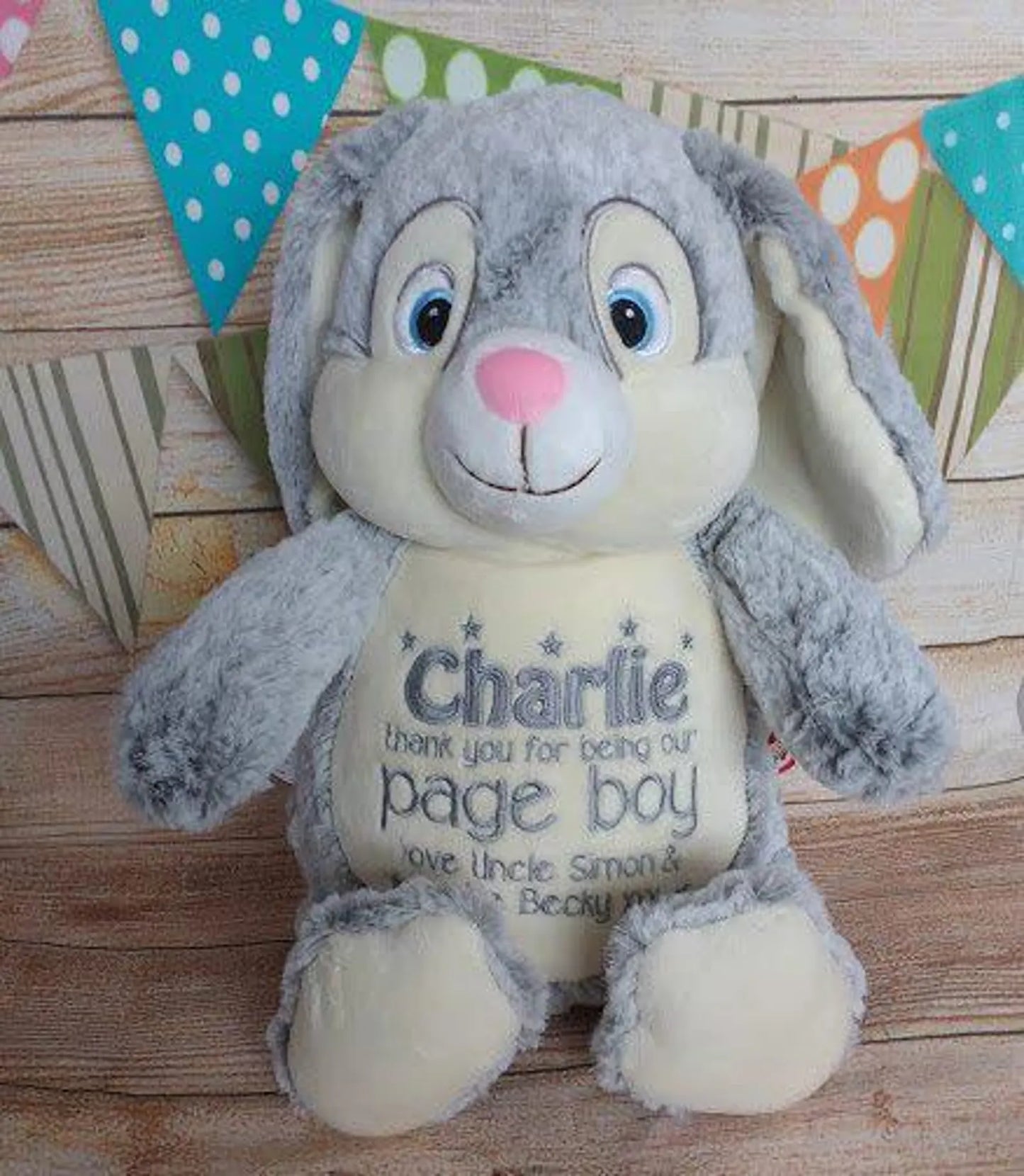Plush toy rabbit with personalized message on a wooden surface with decorative flags in the background