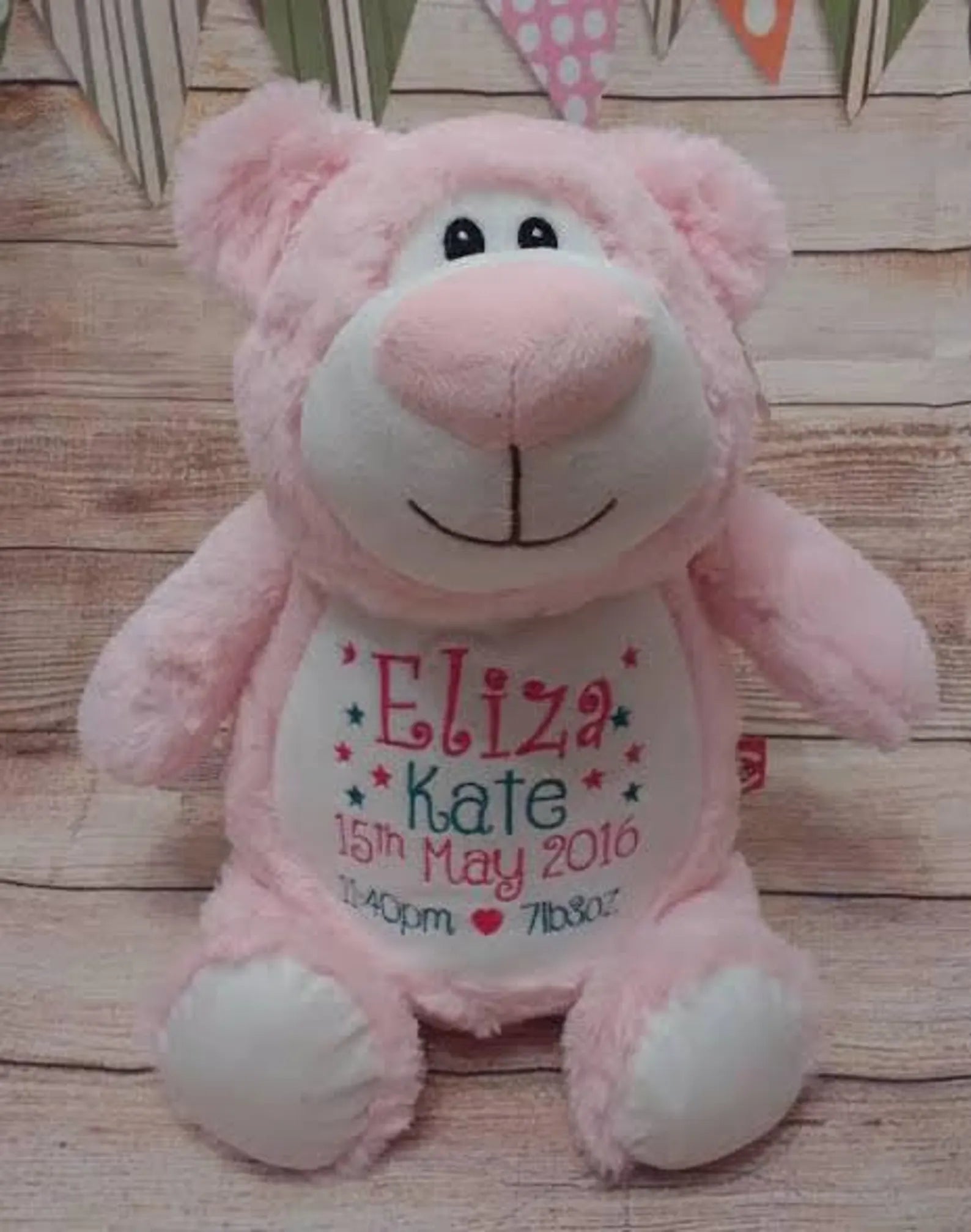 Pink teddy bear with personalized text on a wooden surface