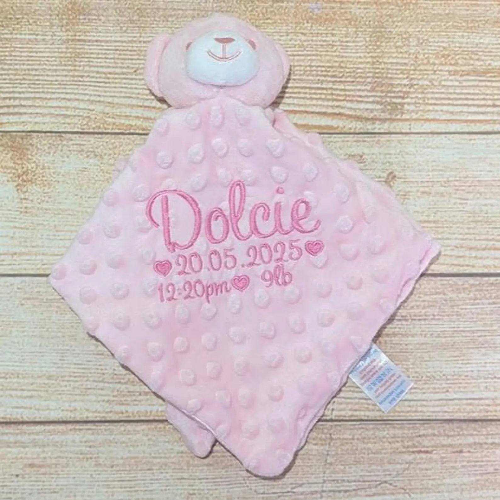 Pink teddy bear security blanket with embroidered details on a wooden surface