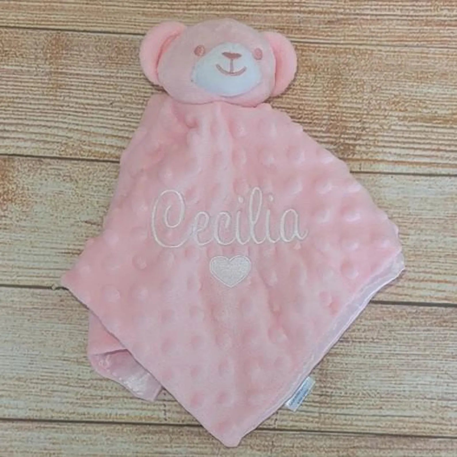 Pink teddy bear security blanket with 'Cecilia' embroidered on a wooden surface