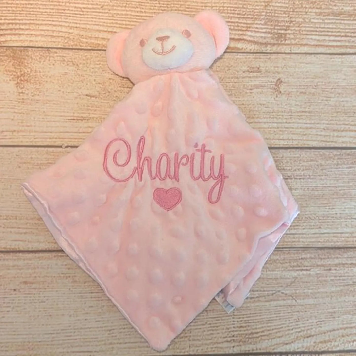 Pink teddy bear security blanket with 'Charity' embroidered on a wooden surface