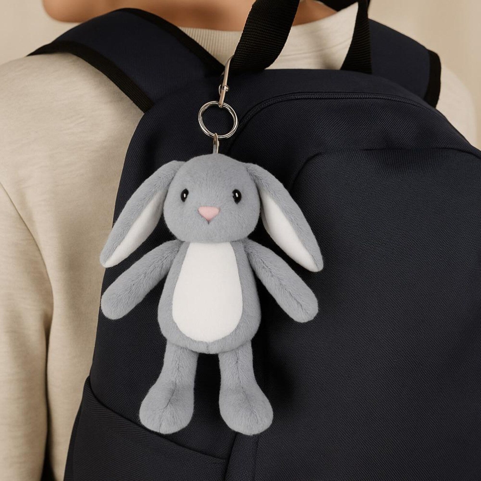Gray plush bunny keychain attached to a black backpack