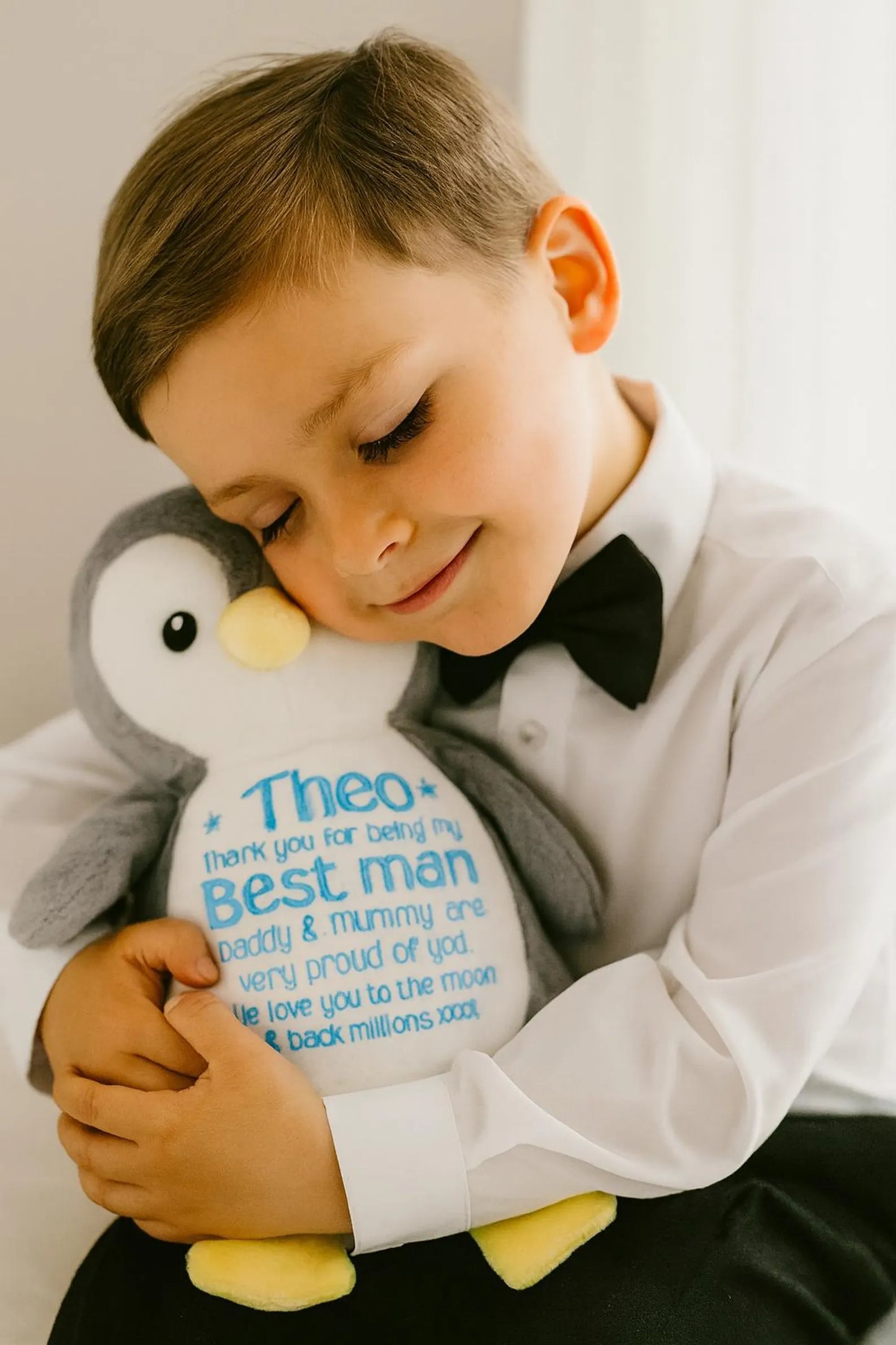 Young boy holding a plush toy with personalized message, wearing a formal outfit.