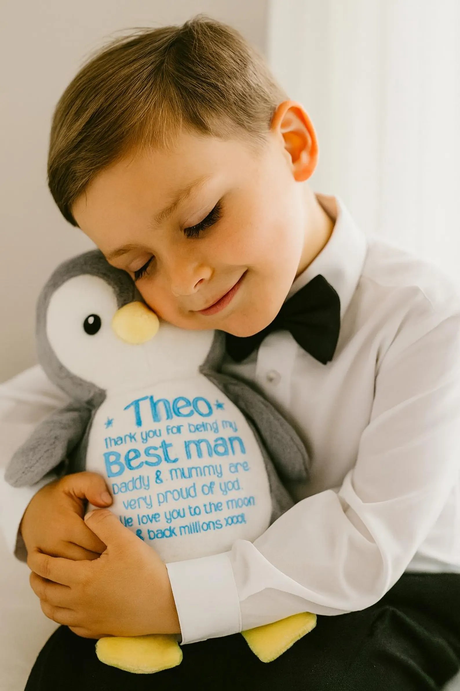 Young boy holding a plush toy with personalized message, wearing a formal outfit.