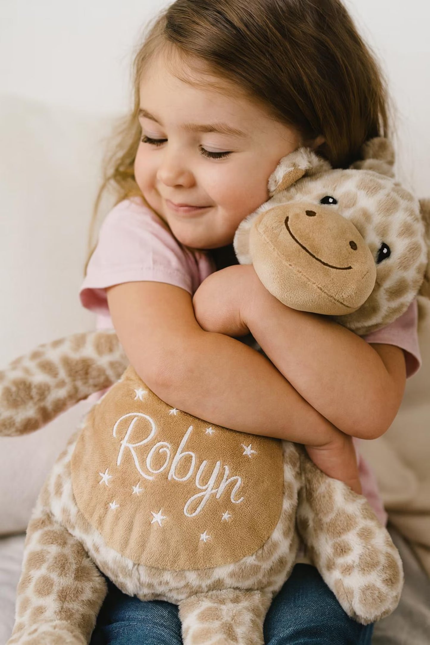 Child hugging a stuffed giraffe toy with 'Robyn' embroidered on it.