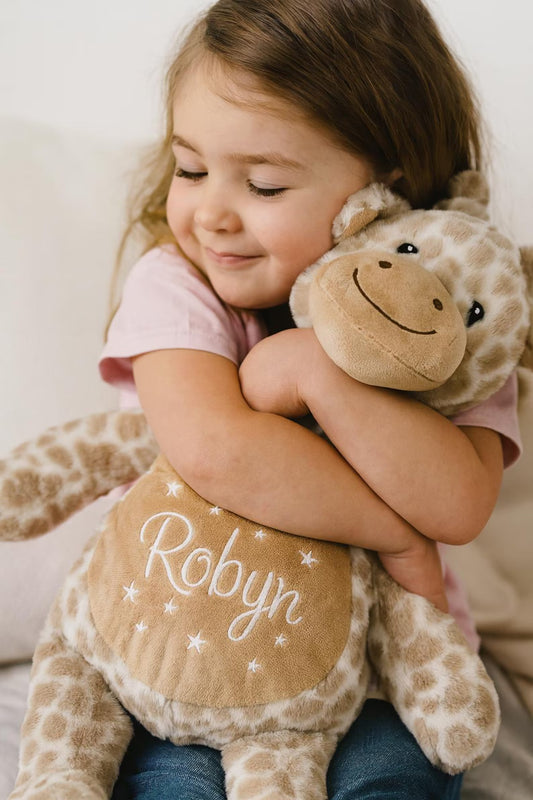 Child hugging a stuffed giraffe toy with 'Robyn' embroidered on it.