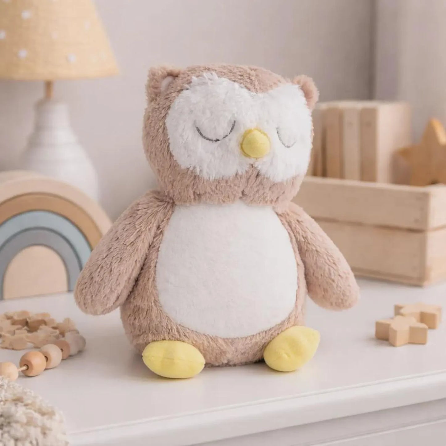 Plush owl toy on a shelf with wooden blocks and a lamp in the background