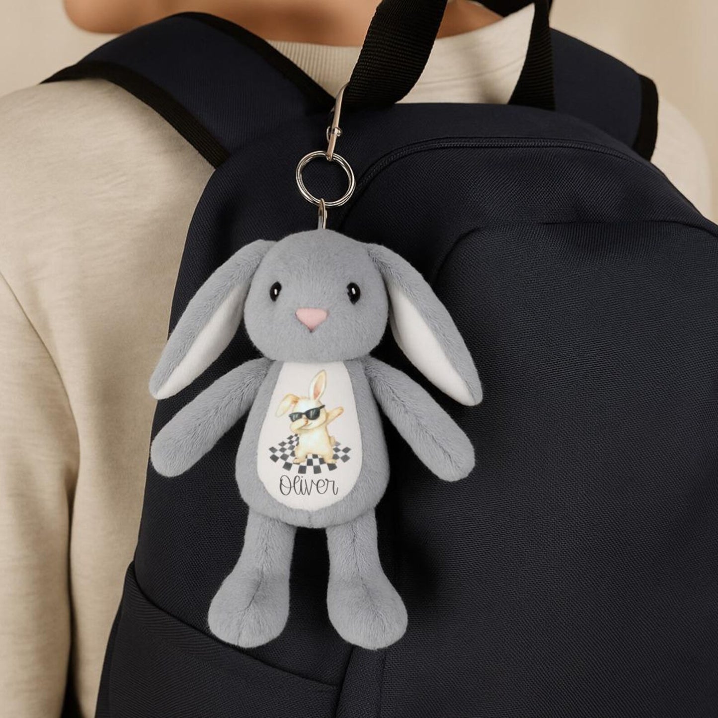 Gray plush bunny keychain attached to a black backpack
