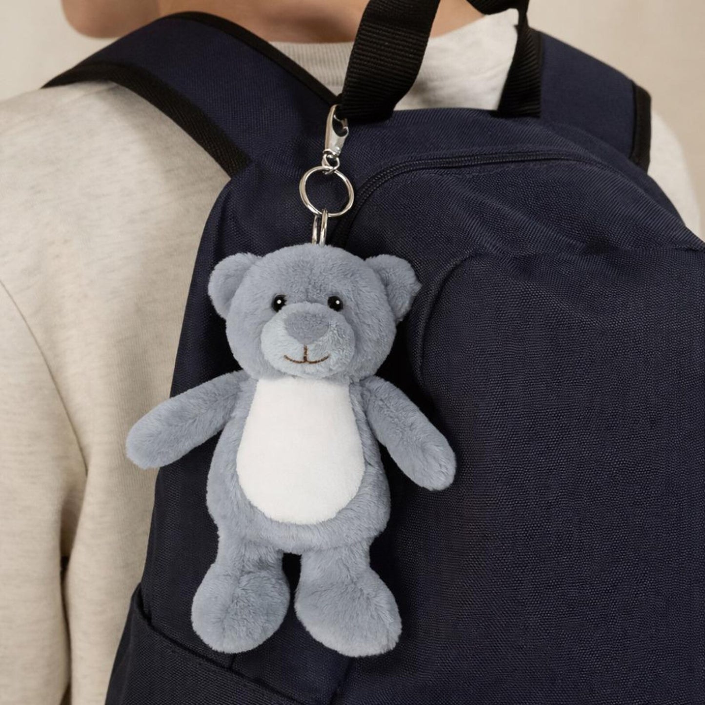 Gray teddy bear keychain attached to a navy backpack