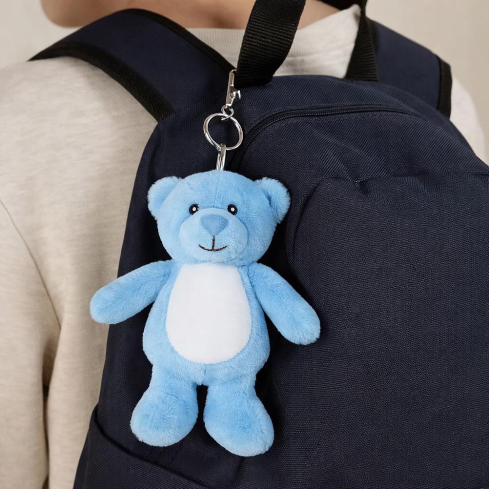 Blue teddy bear keychain attached to a navy backpack