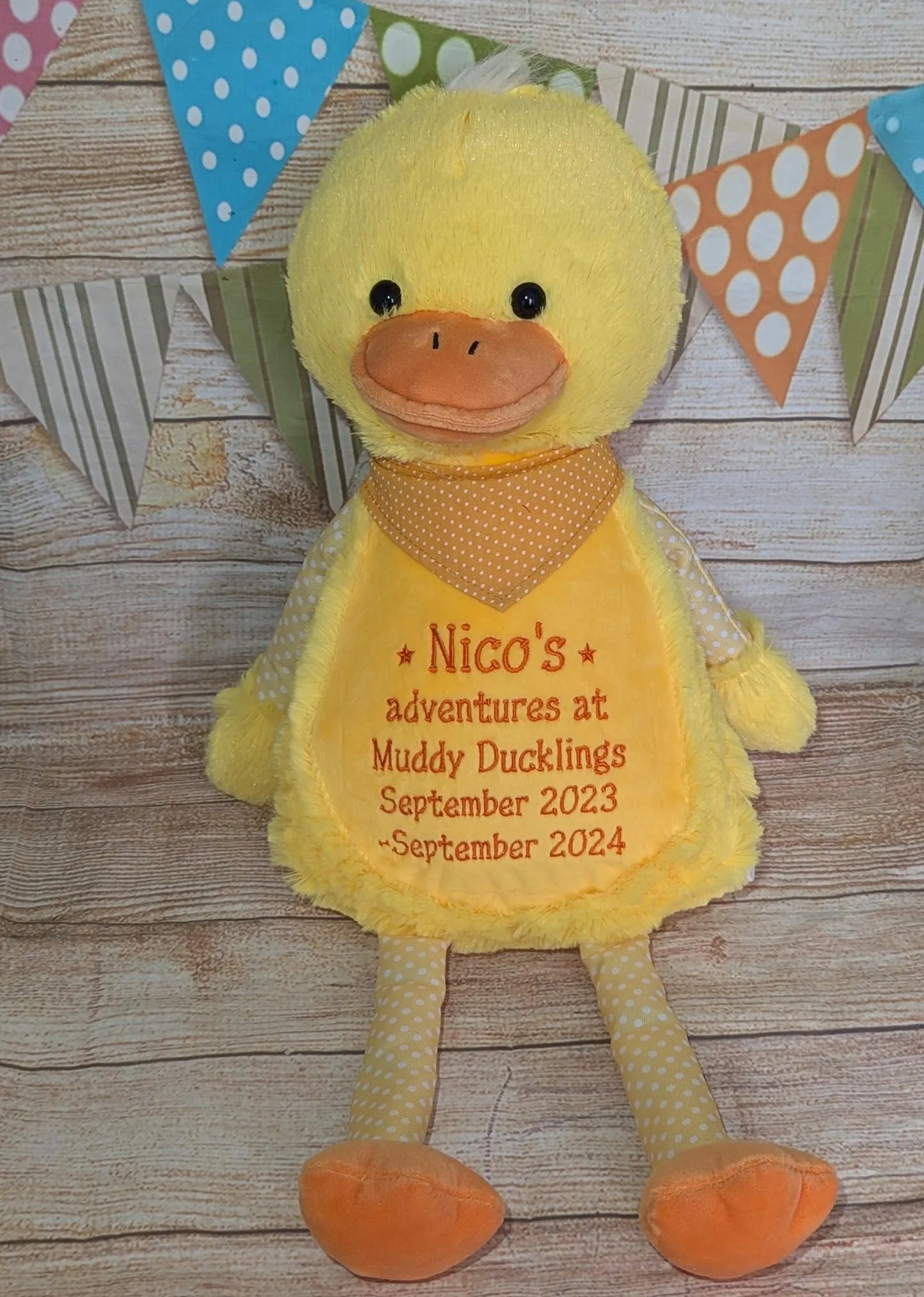 Yellow plush duck toy with text on a wooden surface with decorative flags.
