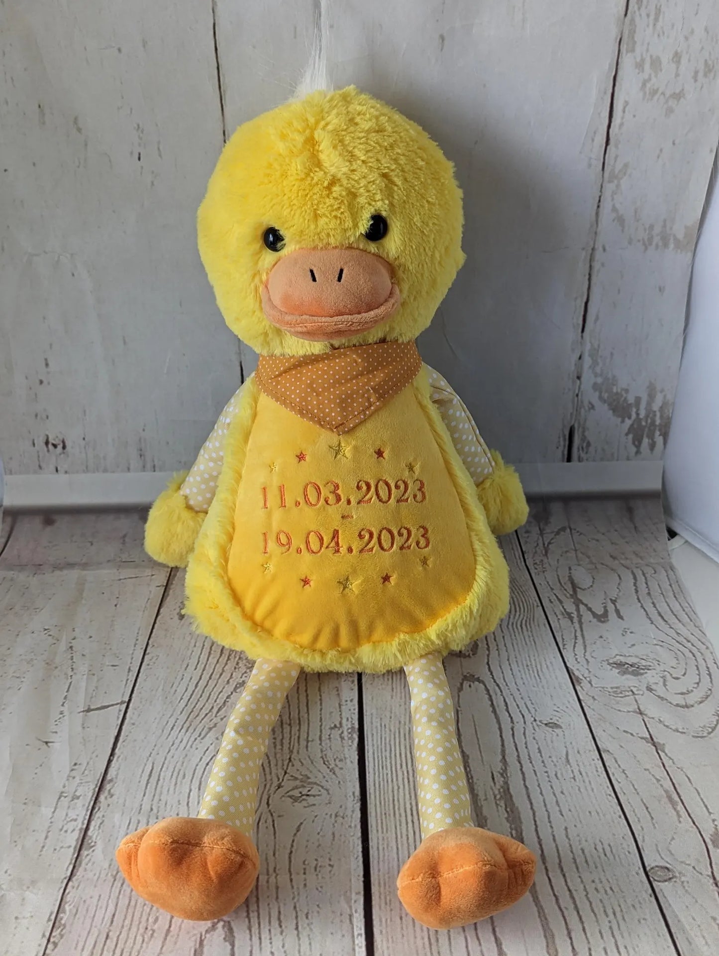 Yellow plush duck toy with embroidered dates on a wooden floor.