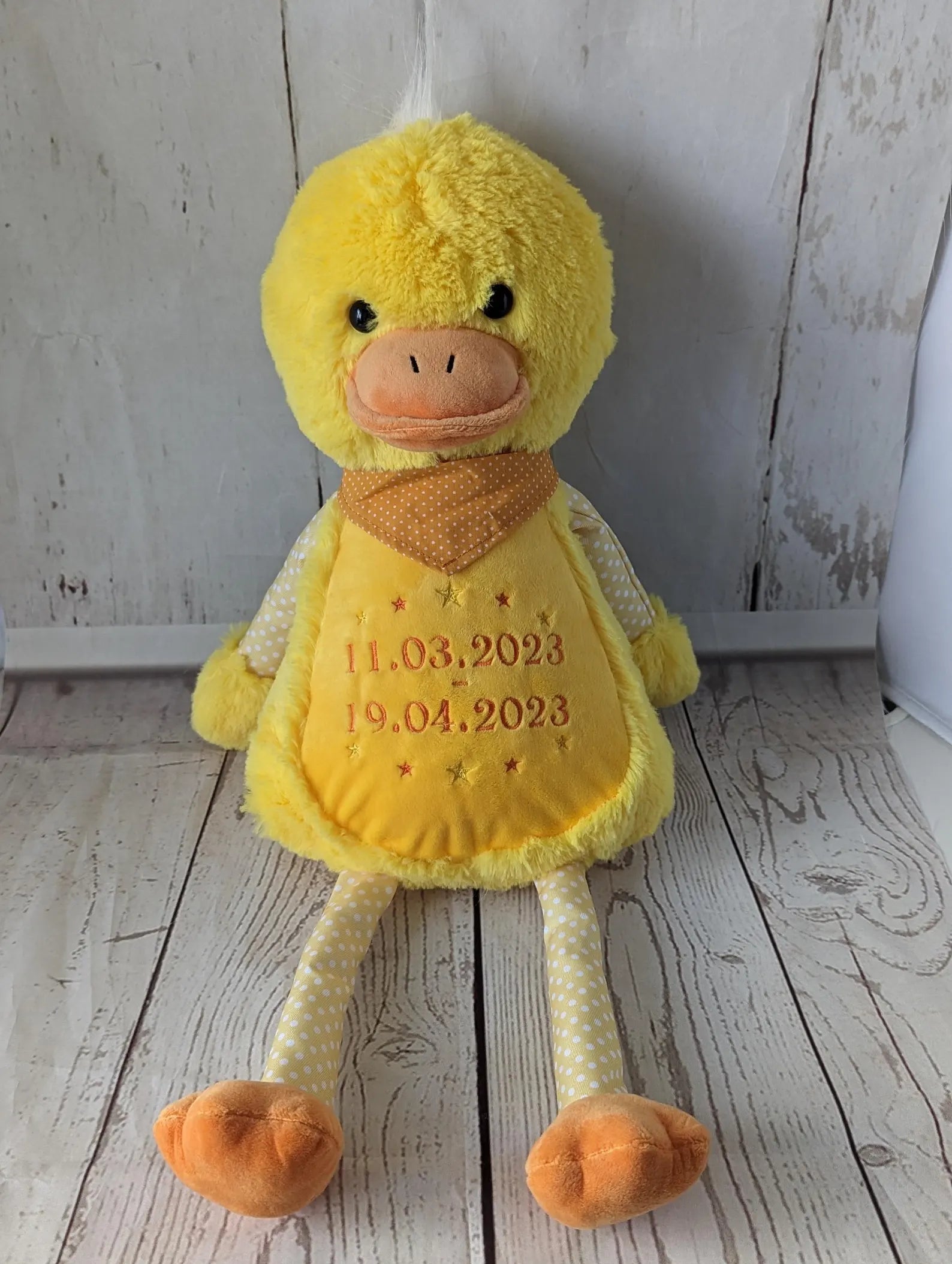 Yellow plush duck toy with embroidered dates on a wooden floor.