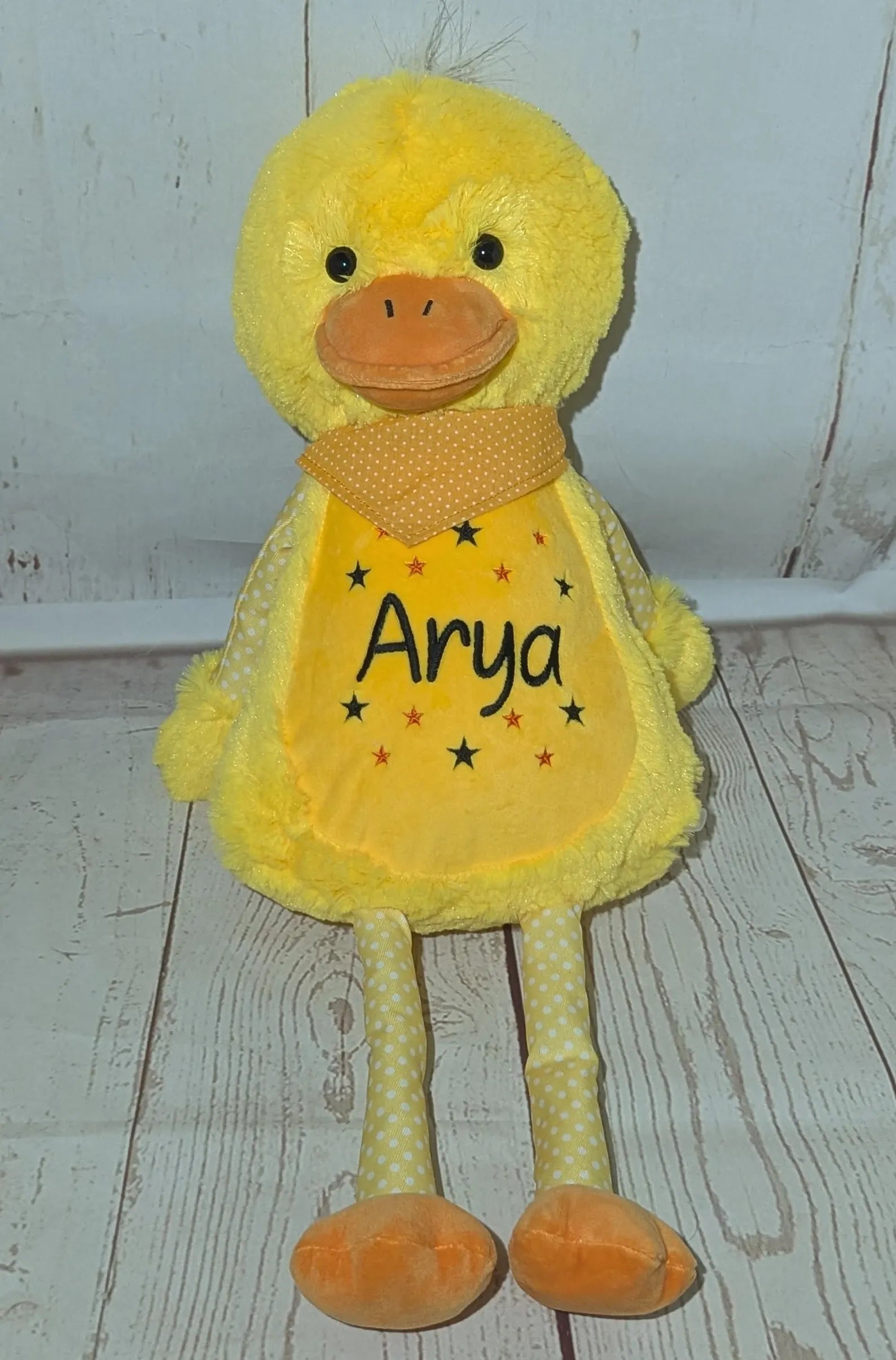 Yellow plush duck toy with 'Arya' on a wooden floor