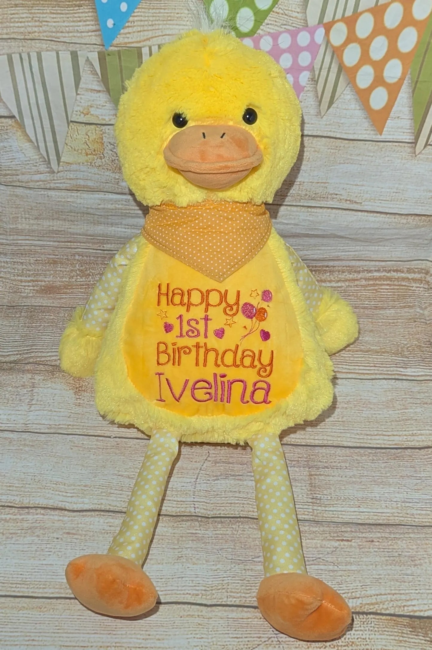 Yellow plush duck with a 'Happy 1st Birthday Ivelina' message on a wooden surface.