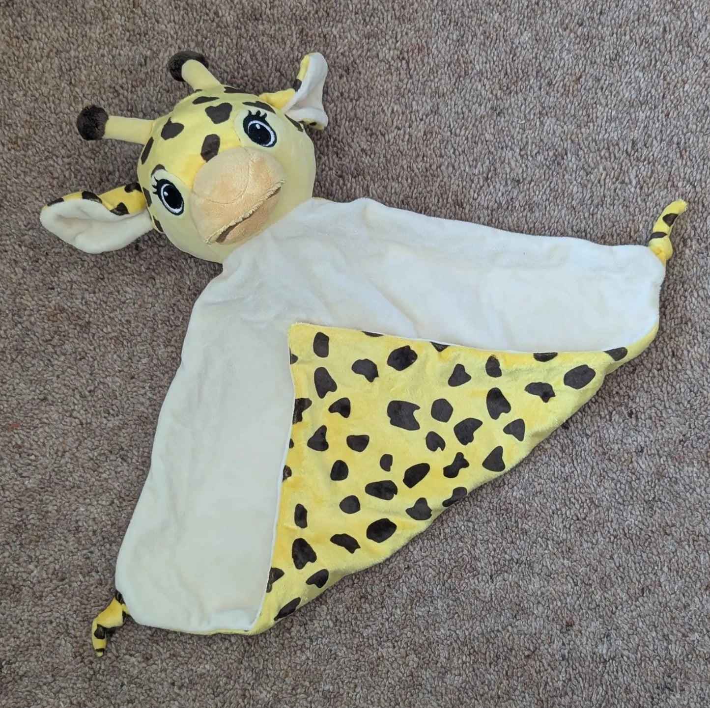 Plush giraffe toy with a white blanket on a brown carpet