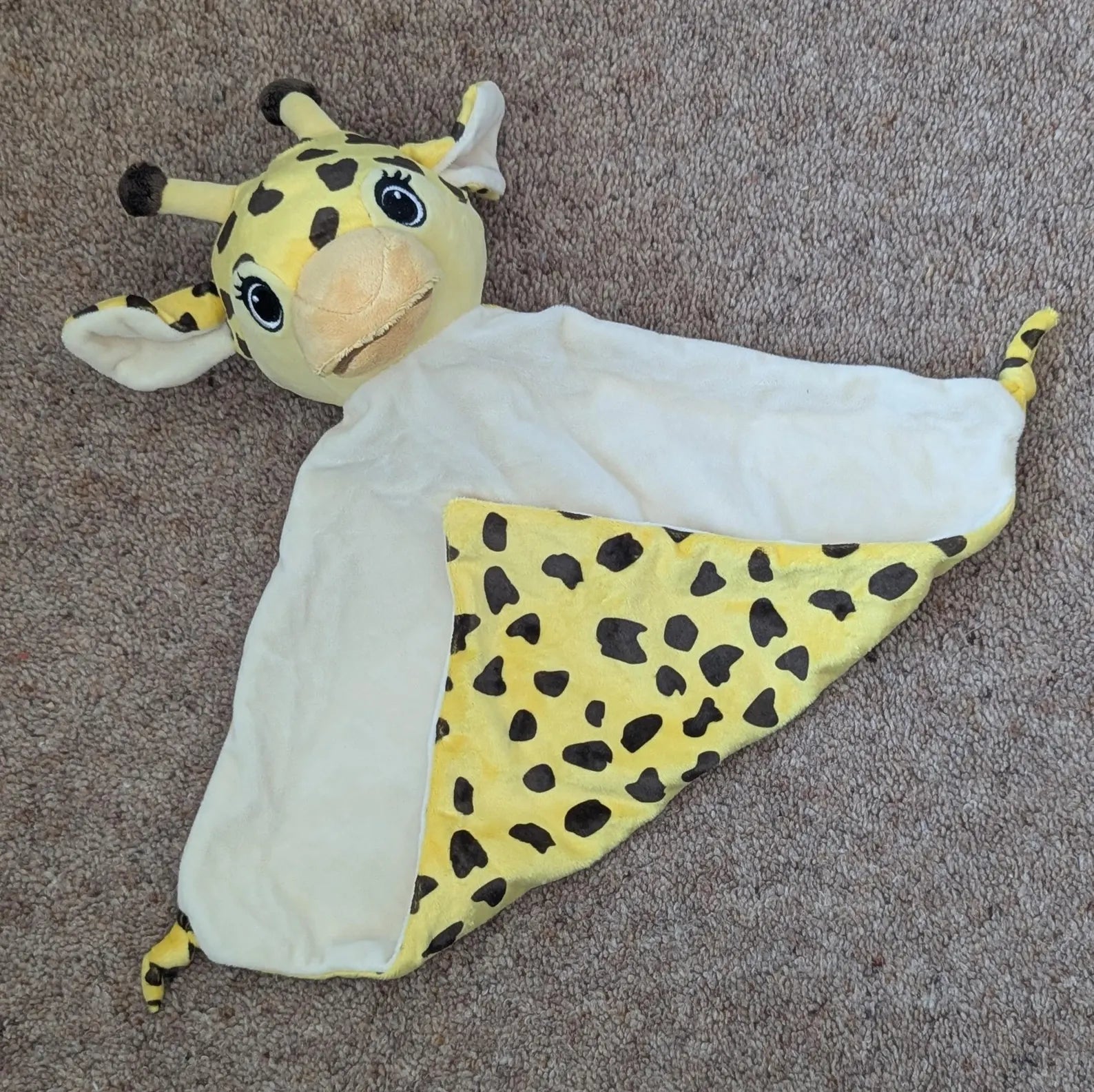 Plush giraffe toy with a white blanket on a brown carpet
