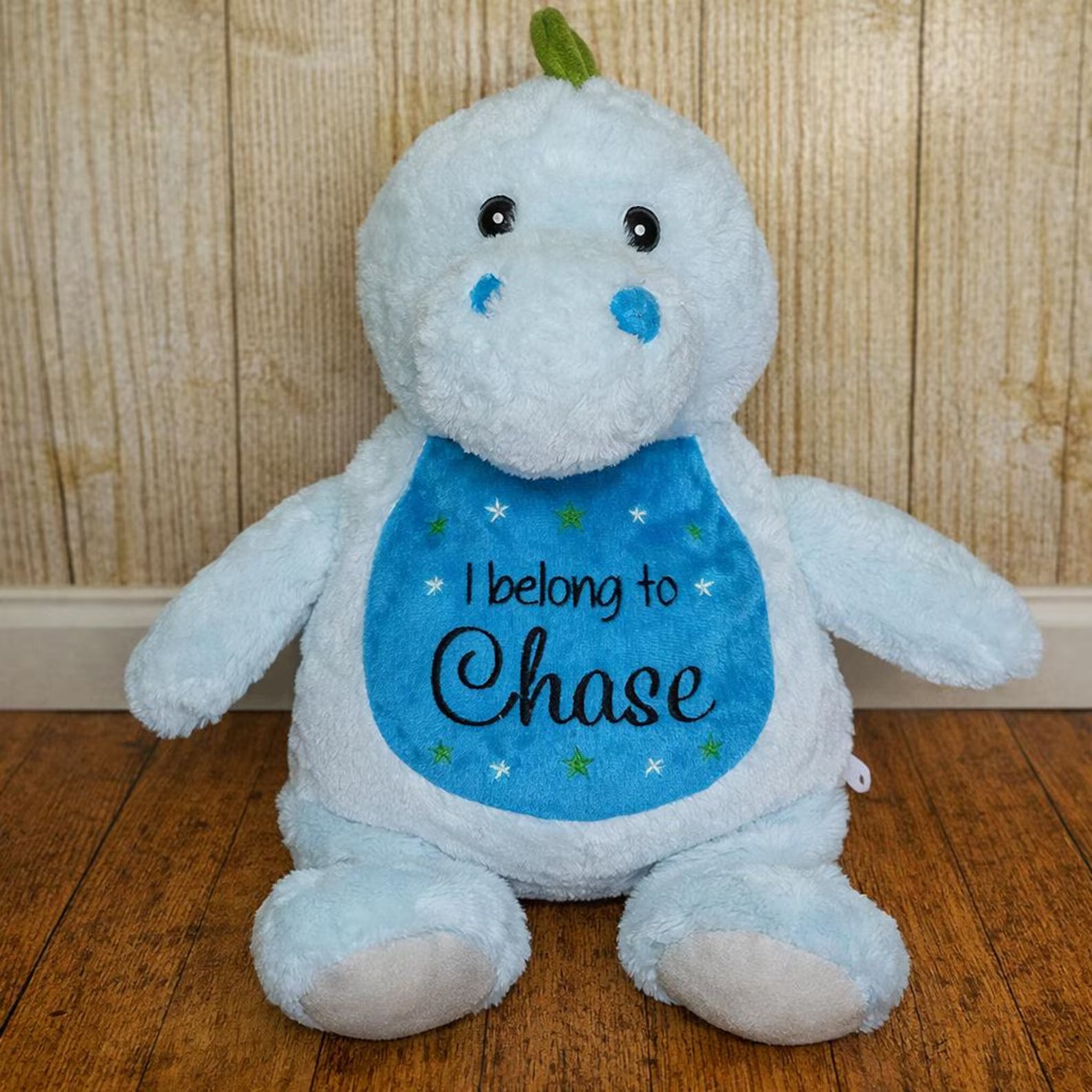 Plush toy with a blue bib that says 'I belong to Chase' on a wooden floor.