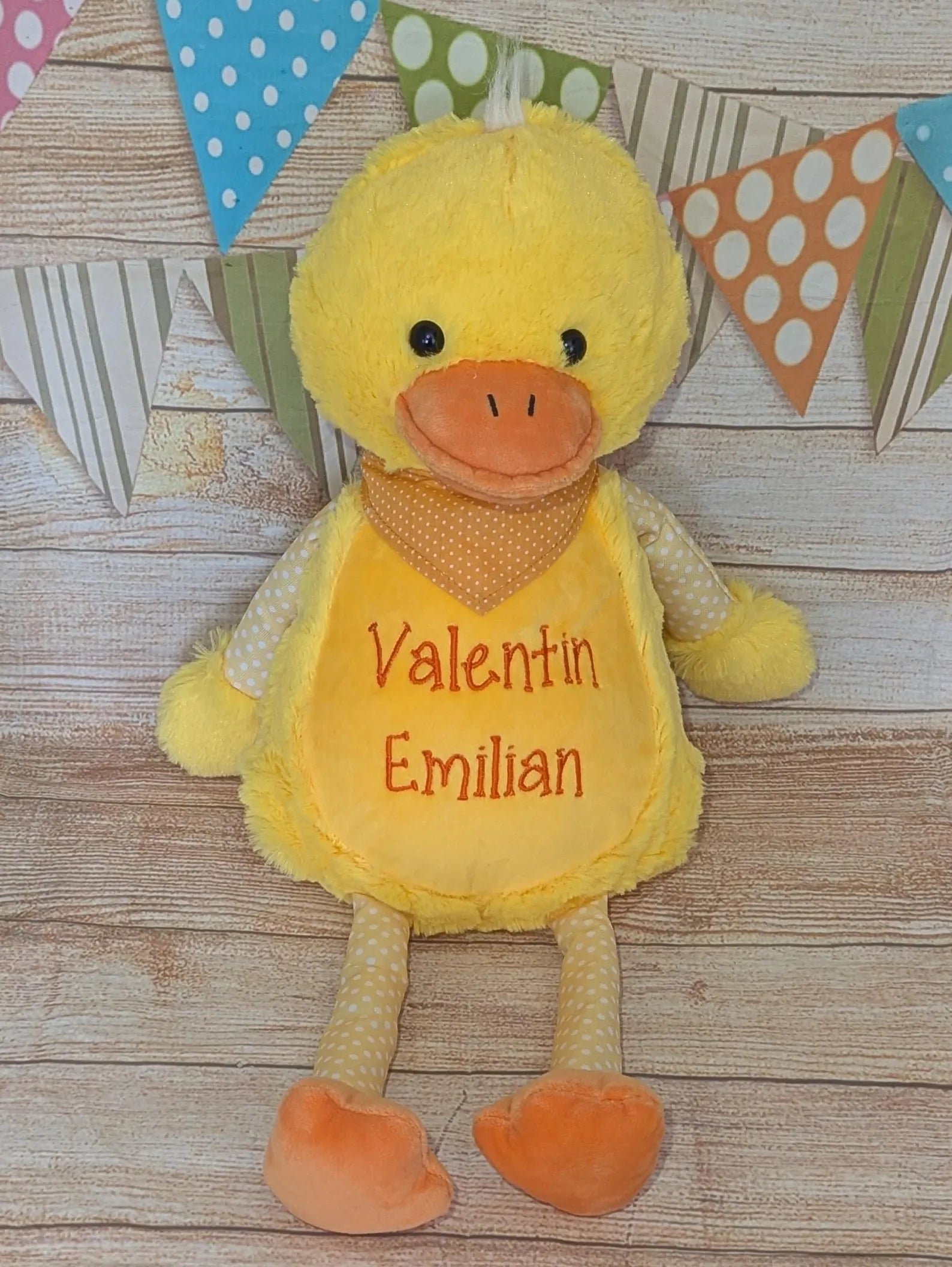 Yellow plush duck with 'Valentin Emilian' on a wooden surface with colorful flags in the background