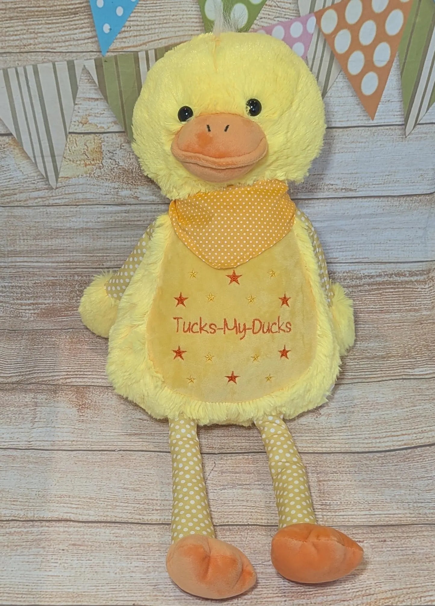 Yellow plush duck toy with a bib on a wooden surface