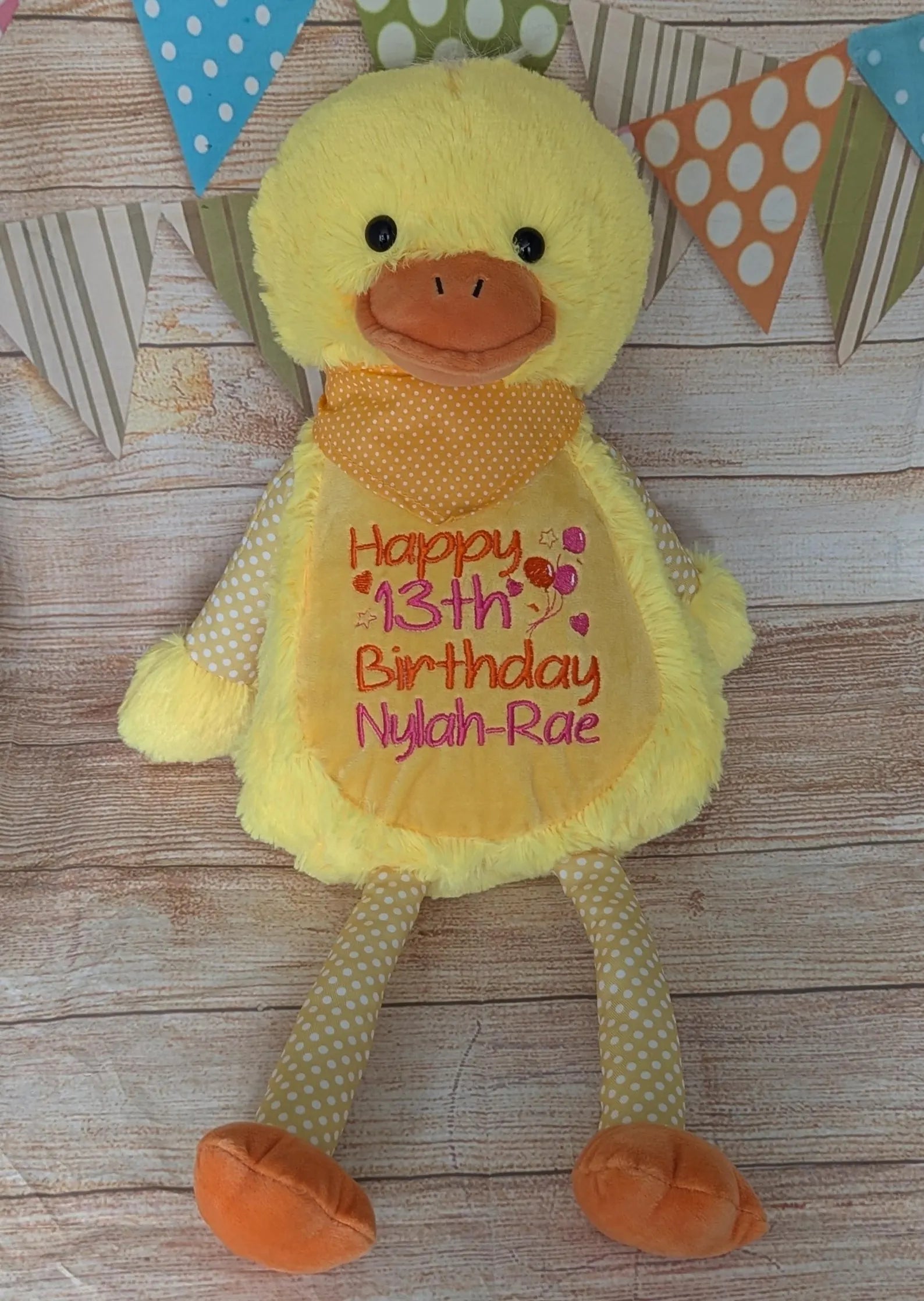 Yellow plush duck with personalized text on a wooden surface with decorative flags.