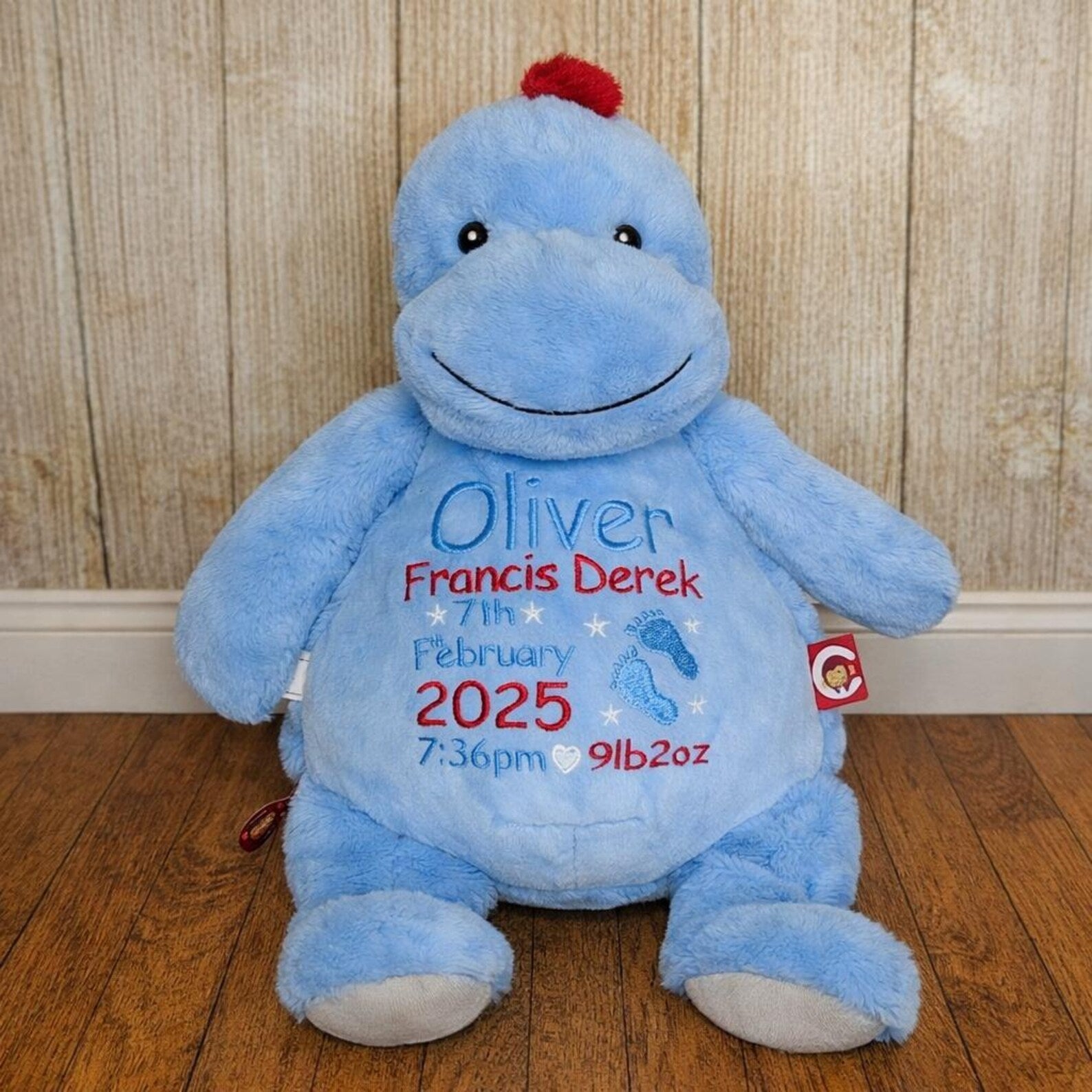 Blue plush toy with personalized text on a wooden floor and wooden wall background
