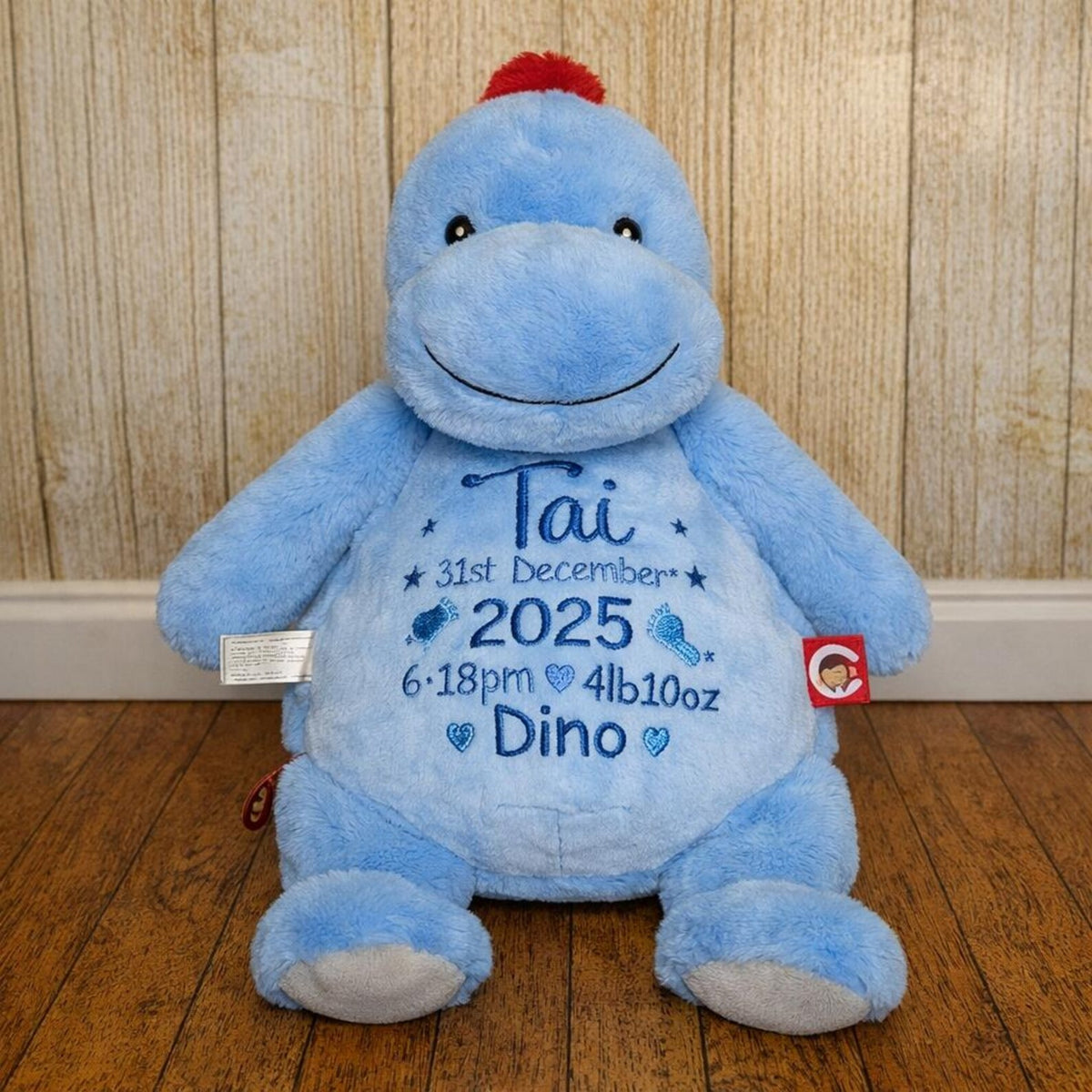 Blue plush dinosaur toy with personalized text on a wooden floor