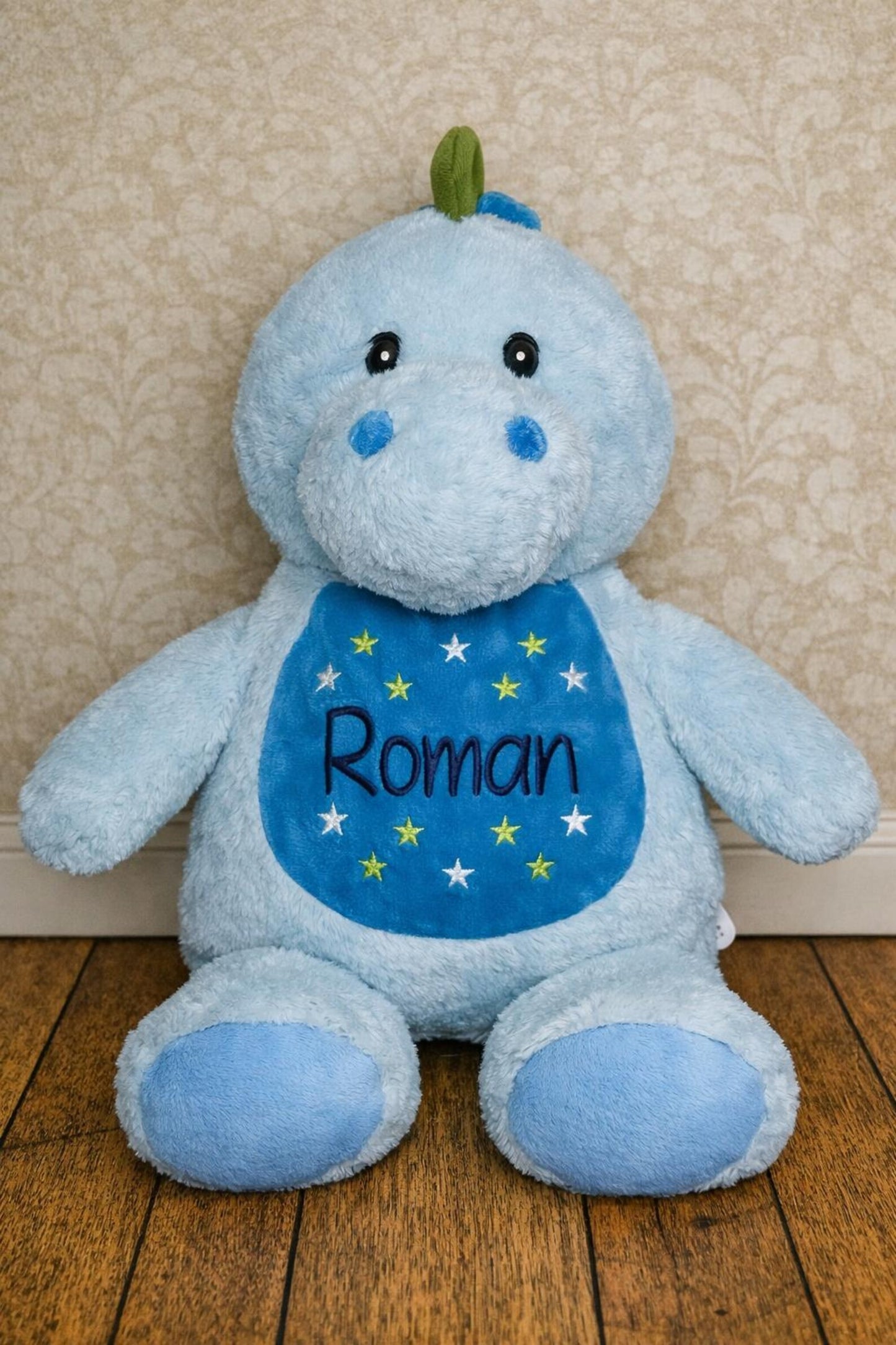 Blue plush toy with 'Roman' on a wooden floor against a beige wall.
