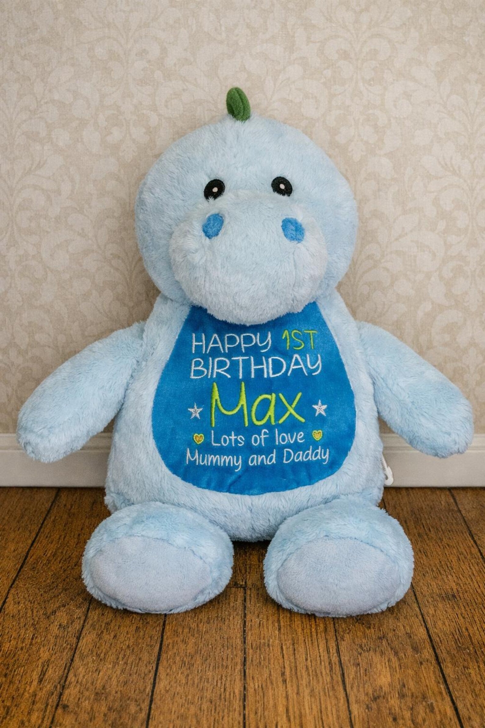 Blue plush toy with a birthday message on a wooden floor against a beige wall.