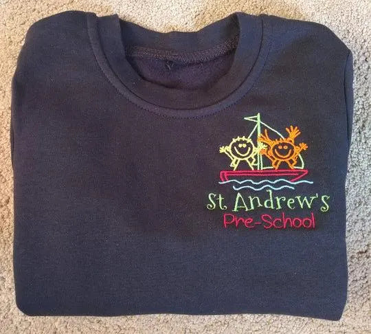 Folded navy blue shirt with 'St. Andrew's Pre-School' logo on a carpeted floor.